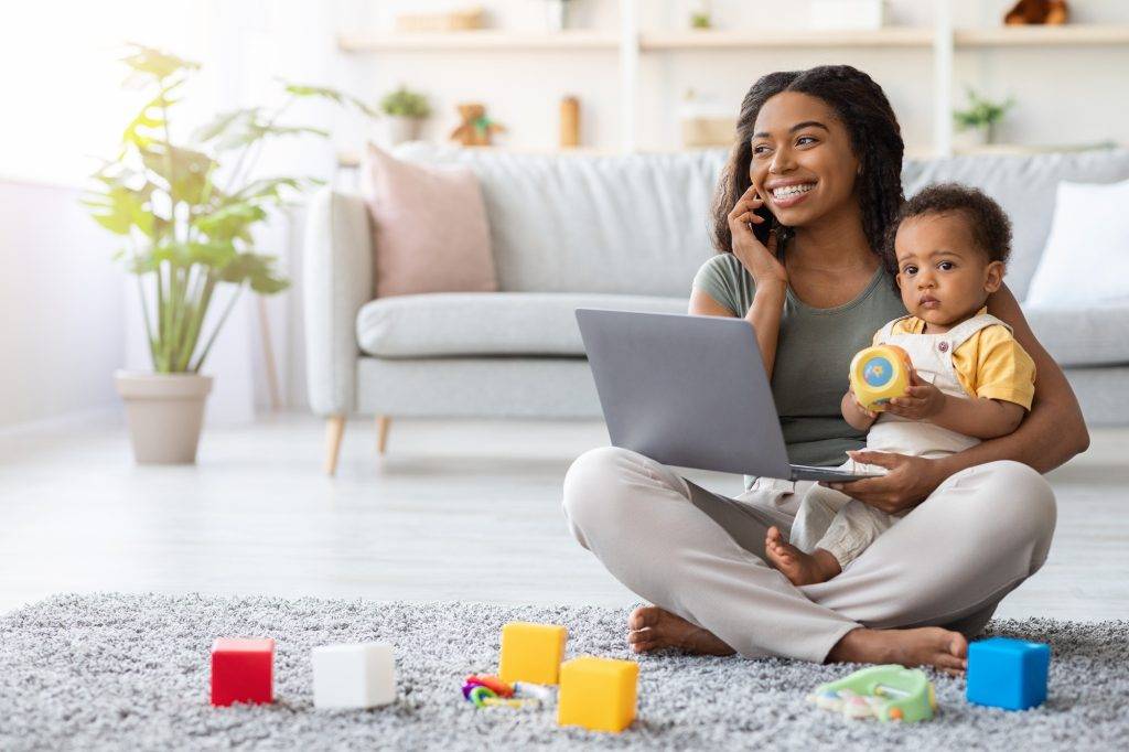 Remote Work With Baby. Black Mom Using Laptop And Talking On Cellphone. Busy Mom's Guide to Unlocking Her Best Self