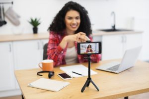 Young woman recording video blog in modern kitchen using smartphone setup