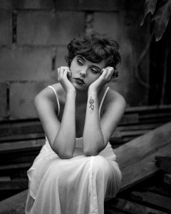 grayscale photo of woman sitting on wooden planks while resting her head on hands